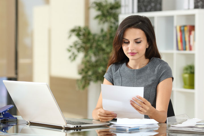 Woman reading a document sitting in front of a computer