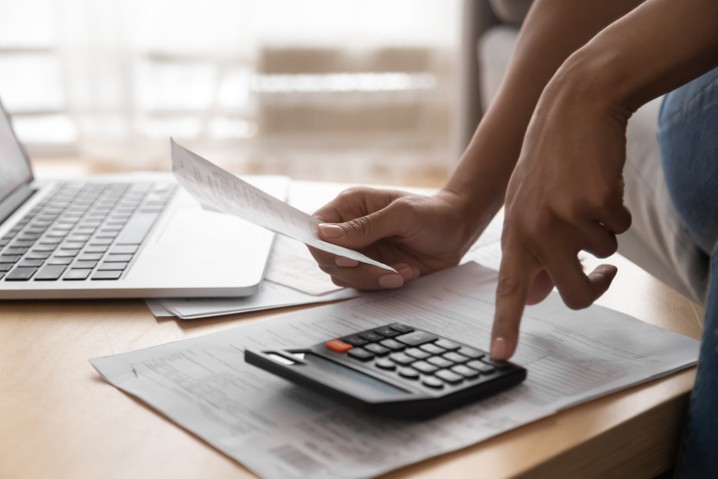 African woman holding in hand paper bills bank receipt using calculator on table