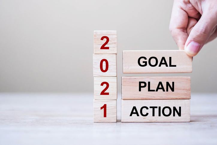 Businessman hand holding wooden cube with text 2021 GOAL, PLAN and ACTION on table background. Resolution, strategy, solution, goal, business and New Year holiday concepts